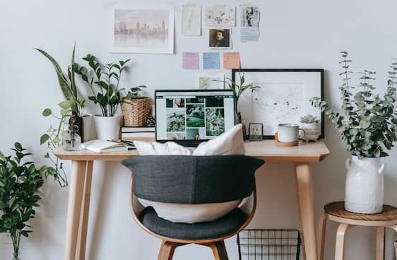 Escritorio de madera con portátil, plantas, tablón de notas adhesivas y una silla gris