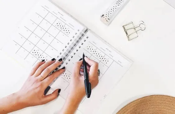 Manos escribiendo con un rotulador en una agenda abierta con calendario mensual