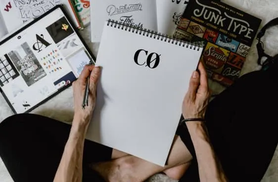 Cuaderno en blanco con el logotipo CØ sobre libros de tipografías y una tableta con ejemplos de letras